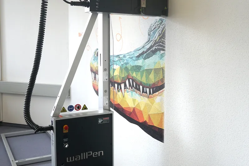 Der fahrbare Wanddrucker steht auf seiner Führungsschiene vor der bedruckten Wand